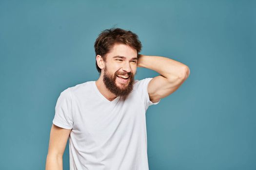 A bearded man in a white T-shirt gestures with his hands emotions blue background. High quality photo