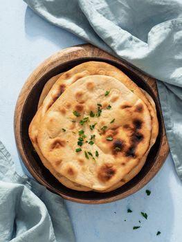 Stack of fesh naan breads in cast-iron pan on blue background with copy space. Top view of perfect naan flatbreads in black circle cast iron pan. Vertical.