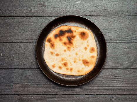 Fresh naan bread in cast-iron pan on dark wooden background with copy space. Top view of perfect naan flatbread black circle cast iron pan
