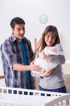 Young parents with their newborn baby near bed cot