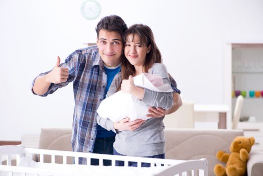 Young parents with their newborn baby near bed cot