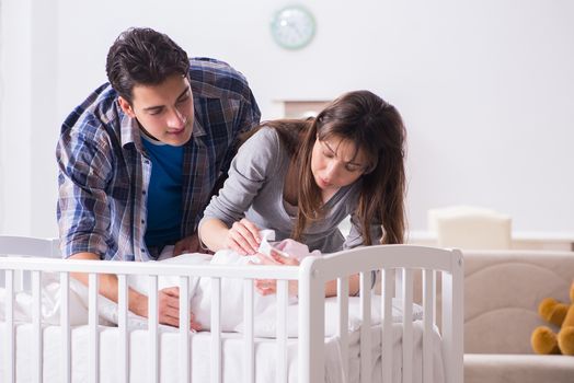 Young parents with their newborn baby near bed cot