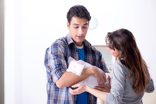 Young parents with their newborn baby near bed cot