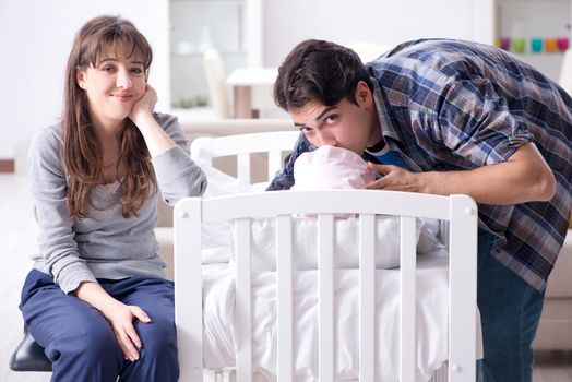 Young parents with their newborn baby near bed cot