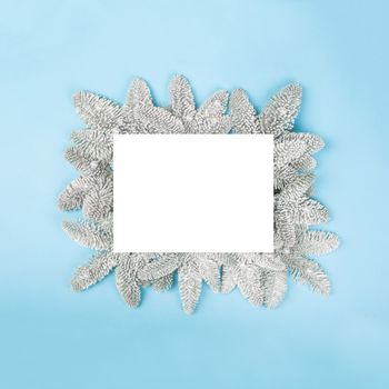 Frosted fir tree twigs and Christmas decorative snowflakes on blue background with white card with copy space for text template flat lay top view design