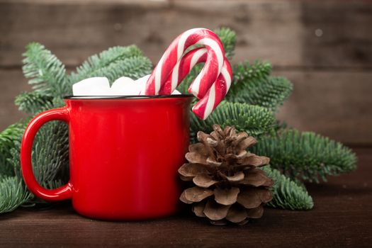 Cocoa in red mug with marshmallows and candy cane and Christmas fir tree on dark wooden background