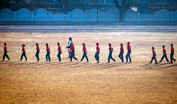 Pune, India:January 6th, 2017-Lady sports teacher guiding children to walk in a formation on playground.