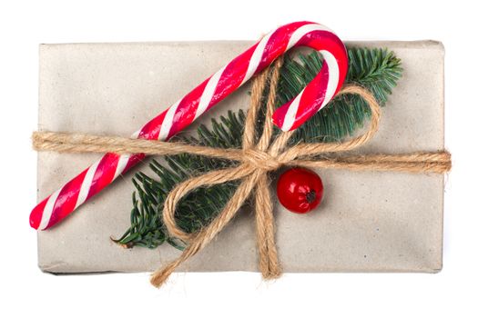 Wrapped vintage christmas gift box in craft paper with rope bow, striped candy cane fir tree twig and red berry isolated on white