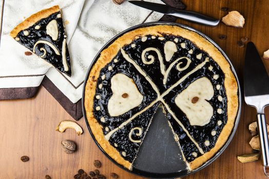 Czech regional traditional hand and home made round pie Chodsky kolac. This one has heart made of quark surounded by plum jam filling. Still life of one slice cut with nuts and fruits around on a wooden table