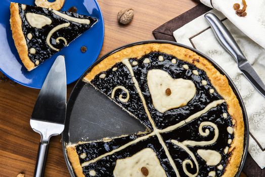 Czech regional traditional hand and home made round pie Chodsky kolac. This one has heart made of quark surounded by plum jam filling. Still life of one slice cut with nuts and fruits around on a wooden table