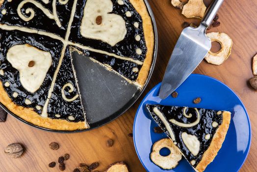 Czech regional traditional hand and home made round pie Chodsky kolac. This one has heart made of quark surounded by plum jam filling. Still life of one slice cut with nuts and fruits around on a wooden table