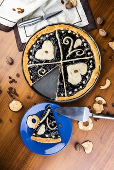 Czech regional traditional hand and home made round pie Chodsky kolac. This one has heart made of quark surounded by plum jam filling. Still life of one slice cut with nuts and fruits around on a wooden table