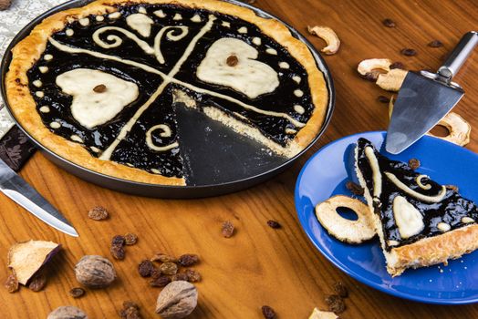 Czech regional traditional hand and home made round pie Chodsky kolac. This one has heart made of quark surounded by plum jam filling. Still life of one slice cut with nuts and fruits around on a wooden table