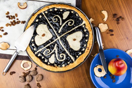 Czech traditional hand and home made round pie Chodsky kolac - speciality of Chodsko region. This one has heart made of quark surounded by plum jam filling. Still life with nuts and fruits on a wooden table