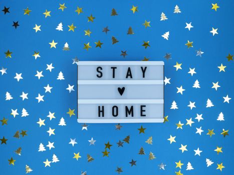 Light box with Stay home quote on blue background with confetti. Christmas quarantine.