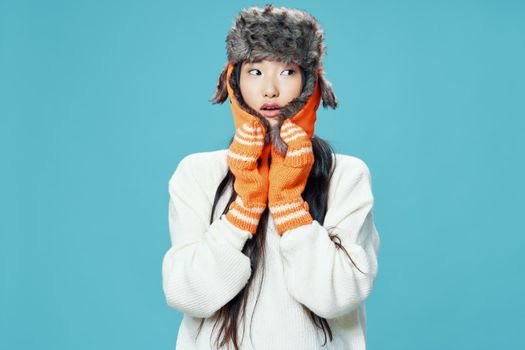 Asian woman in warm caps on a blue background looks to the side