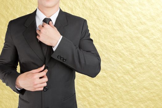 Well dressed businessman looklike smart adjusting  his neck tie on gold background : fill text