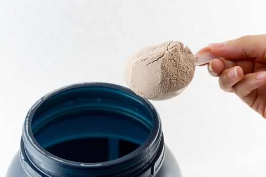 The hand raise a spoon measure Whey protein chocolate powder for fitness and bodybuilding gaining muscle.