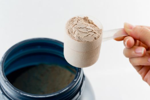 The hand raise a spoon measure Whey protein chocolate powder for fitness and bodybuilding gaining muscle.