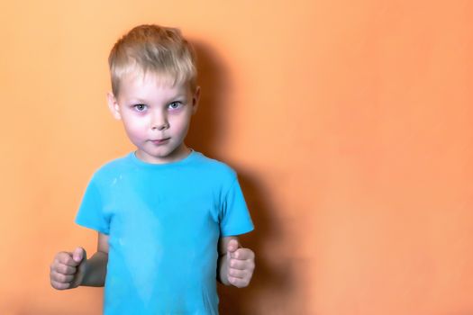 boy in a blue t shirt on a pink background looks at the camera lens clenching his fists