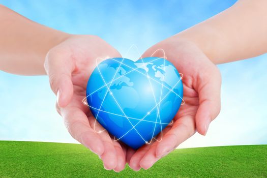 Female hands holding on earth global heart on grassland.