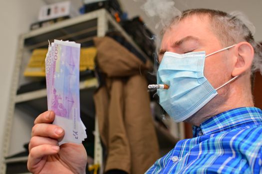 Man in the workplace smokes a cigarette through a medical mask and counts money
