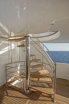 Wooden curved spiral staircase on sundeck area of large luxury motor yacht