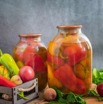 In glass jars, canned bell peppers, next to a box of peppers and other vegetables. Front view, close-up, copy space