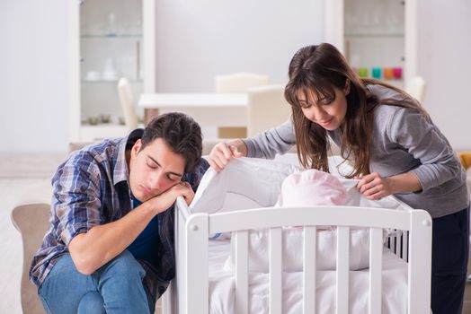 Young parents with their newborn baby near bed cot