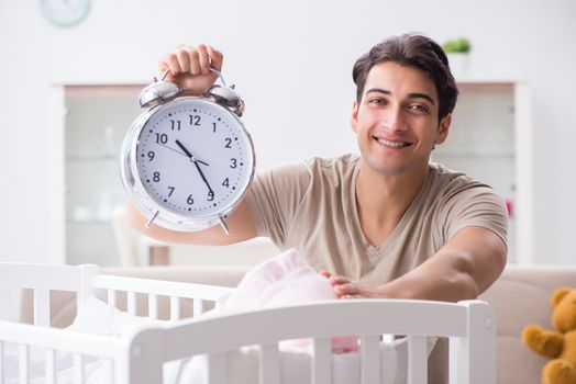 Young dad with clock near newborn baby bed cot