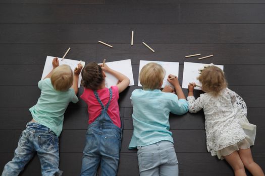 Happy children. Top view creative photo of little boys and girls on brown wooden floor. Children lying and drawing with pencils