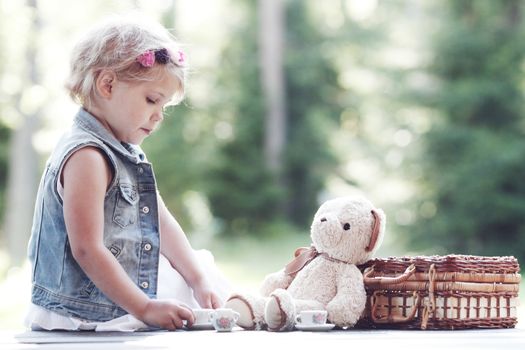 Pretty girl playing with teddy bear outdoors, drinking tea