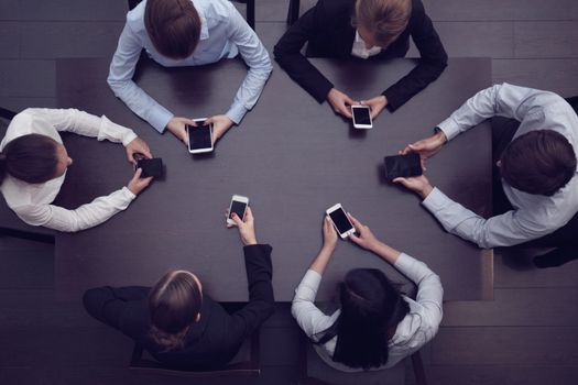 Business people with smart phones sitting around the table, top view