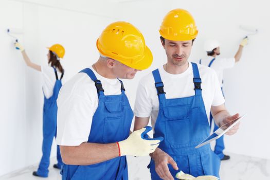 Workers in blue uniform and yellow hardhats with blueprint working at construction site