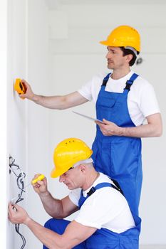 Electrician working with cable inside house, foreman measuring wall