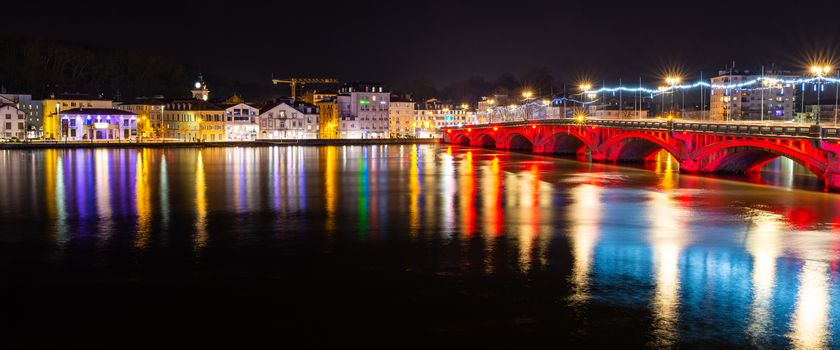 BAYONNE, FRANCE - CIRCA DECEMBER 2019: Saint-Esprit bridge and neighbourhood at night and reflecting on the river Adour.