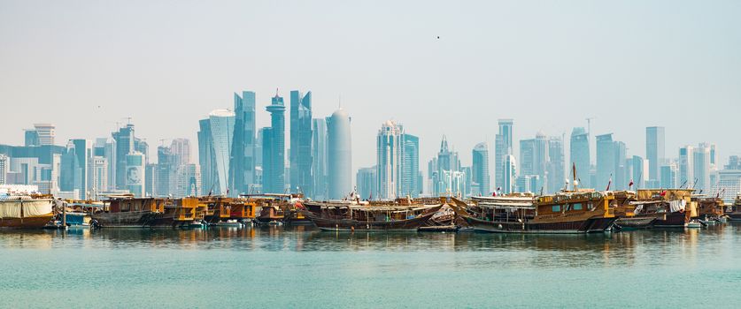 DOHA, QATAR - CIRCA AUGUST 2019: Midday view of Doha cityscape with traditional dhow boats in the foreground