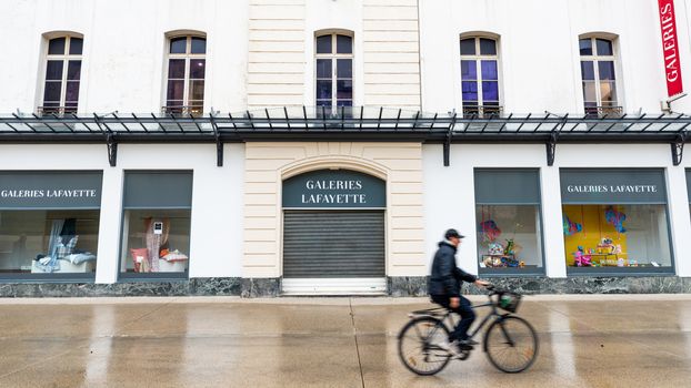 BAYONNE, FRANCE - MARCH 16, 2019: A cyclist passes by the Galeries Lafayette store which is closed because of the outbreak of Coronavirus and the subsequent lockdown.