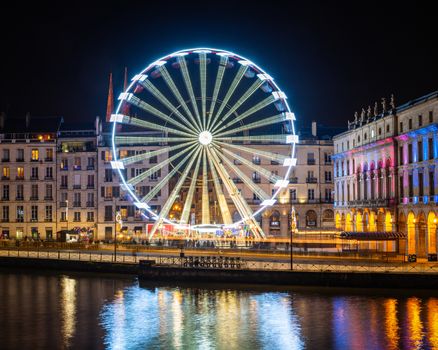 BAYONNE, FRANCE - DECEMBER 28, 2019: The ferris wheel at night. Bayonne city hall illuminated on the right hand side.