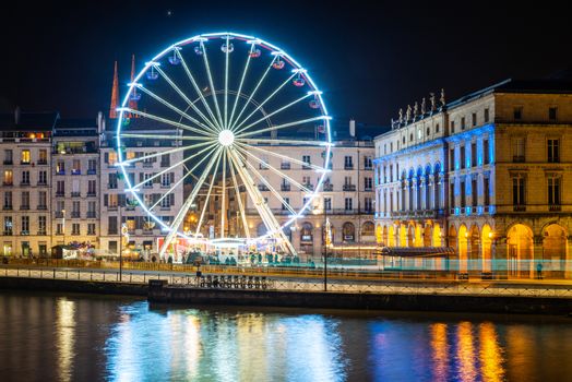 BAYONNE, FRANCE - DECEMBER 28, 2019: The ferris wheel at night. Bayonne city hall illuminated on the right hand side.