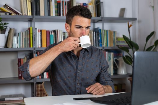 Handsome male businessman working on laptop and drinking tea from home