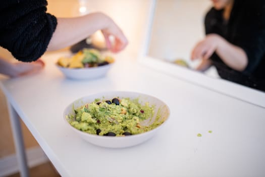 Bowl of guacamole sauce with olives on a white table and in front of a mirror. Traditional Mexican avocado sauce on a table. Spicy Mexican cuisine