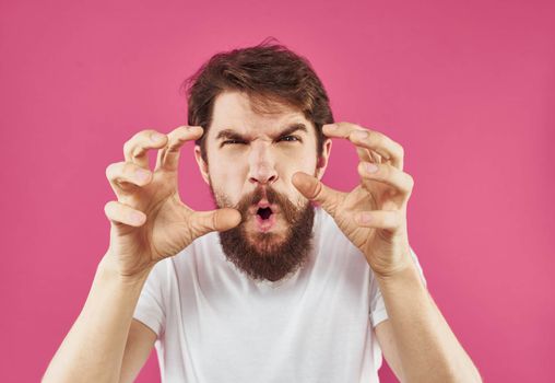 A man with a beard gestures with his hands near his face on a pink background. High quality photo