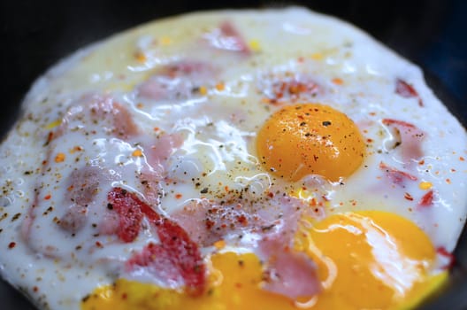 Closeup of ham and eggs with pepper seasoning in the pan.
