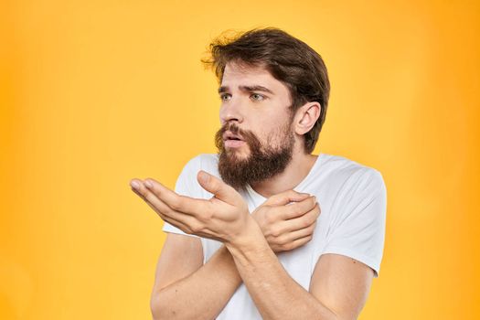 A man in a white t-shirt gestures with his hands studio lifestyle yellow background emotions. High quality photo