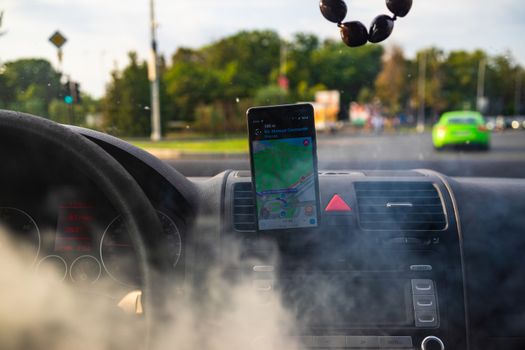 In car dashboard view with smartphone showing Waze maps to show the way thru the city. Driver using Waze maps in Bucharest, Romania, 2020