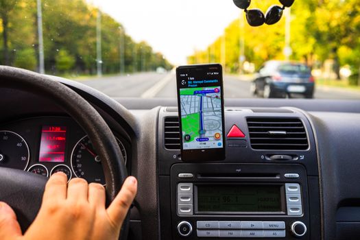 In car dashboard view with smartphone showing Waze maps to show the way thru the city. Driver using Waze maps in Bucharest, Romania, 2020