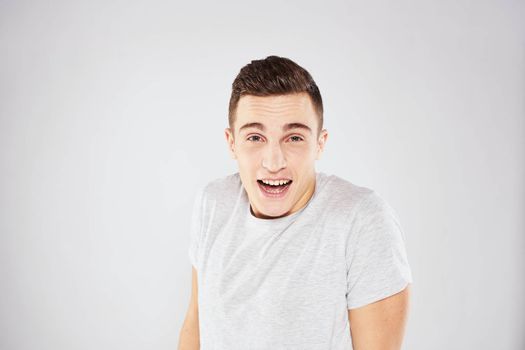 Man in a white t-shirt emotions gestures with hands close-up cropped view light background. High quality photo