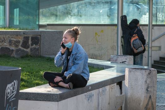 A young woman is talking on her phone close to Hradcanska tram stop during quarantine. This is a lockdown period in the Czech Republic due to the increase of COVID-19 infectious in the country. Hradcanska tram stop it is in Prague 6