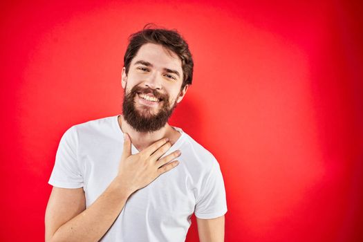 A man in a white T-shirt with a beard gestures with his hands emotions red background. High quality photo